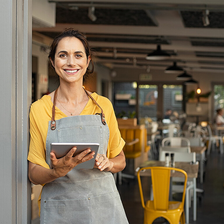 Eine lächelnde Frau in einer Restaurant-Filiale arbeitet an einem Tablet.